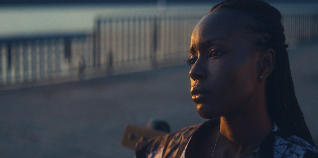 An image from the film Nanny. It features a woman (Anna Diop) standing outside. She has a blank expression on her face. 