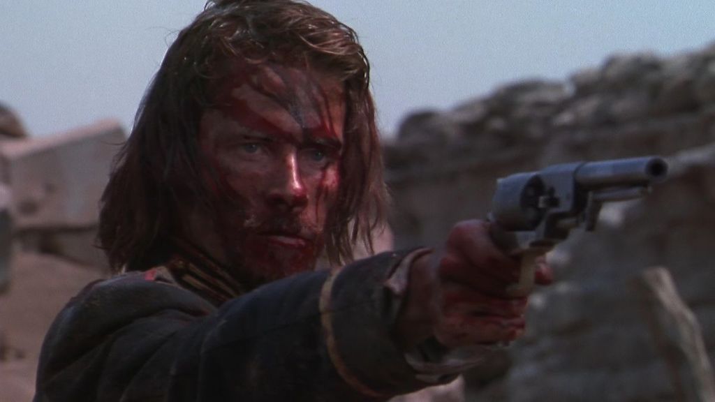 An image from the film Ravenous. It features a military captain (Guy Pearce), he is aiming a pistol in front of himself and has blood all over his face. 