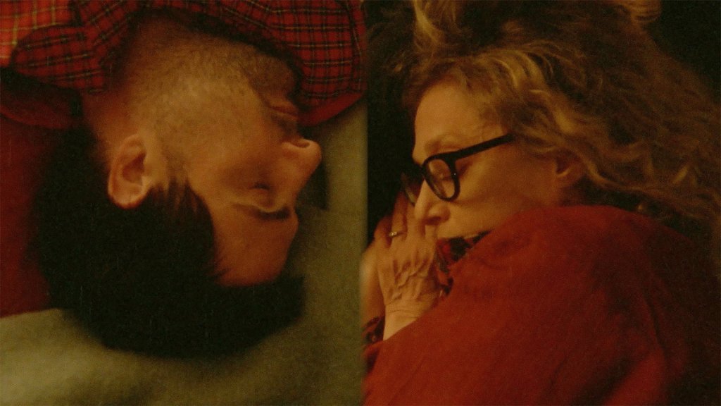 An image from the film Between the Temples. It features a man (Jason Schwartzman) and a woman (Carol Kane) in a split screen, they are each sleeping with their heads tilted to the side.