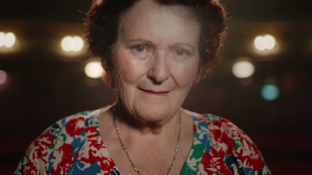 An image from the documentary film Housewife of the Year. It features a close up of an older woman on a theatre stage.
