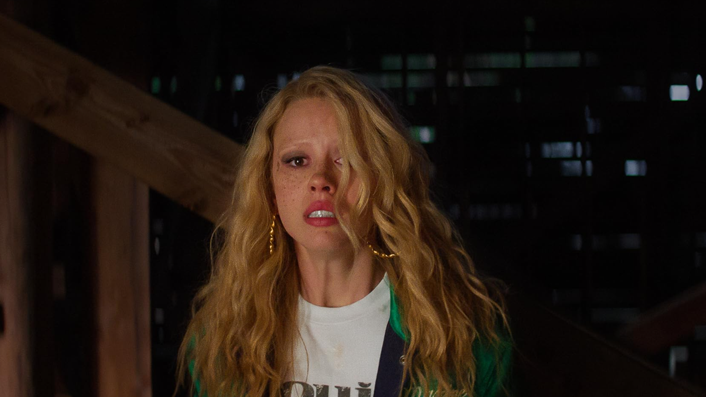 An image from the film MaXXXine. It features a woman (Mia Goth) looking startled. Some of her hair is hanging in front of her face.