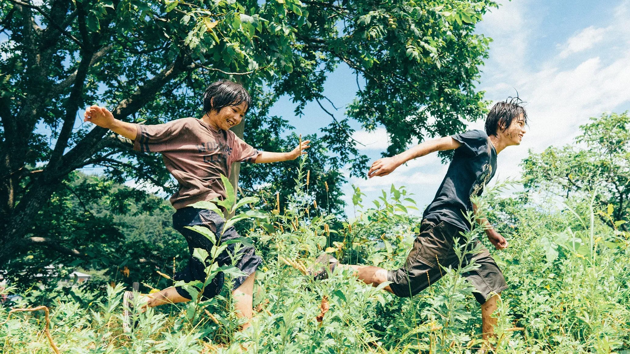 An image from the film Monster. It features two young boys running through a field with tall plants and grass.