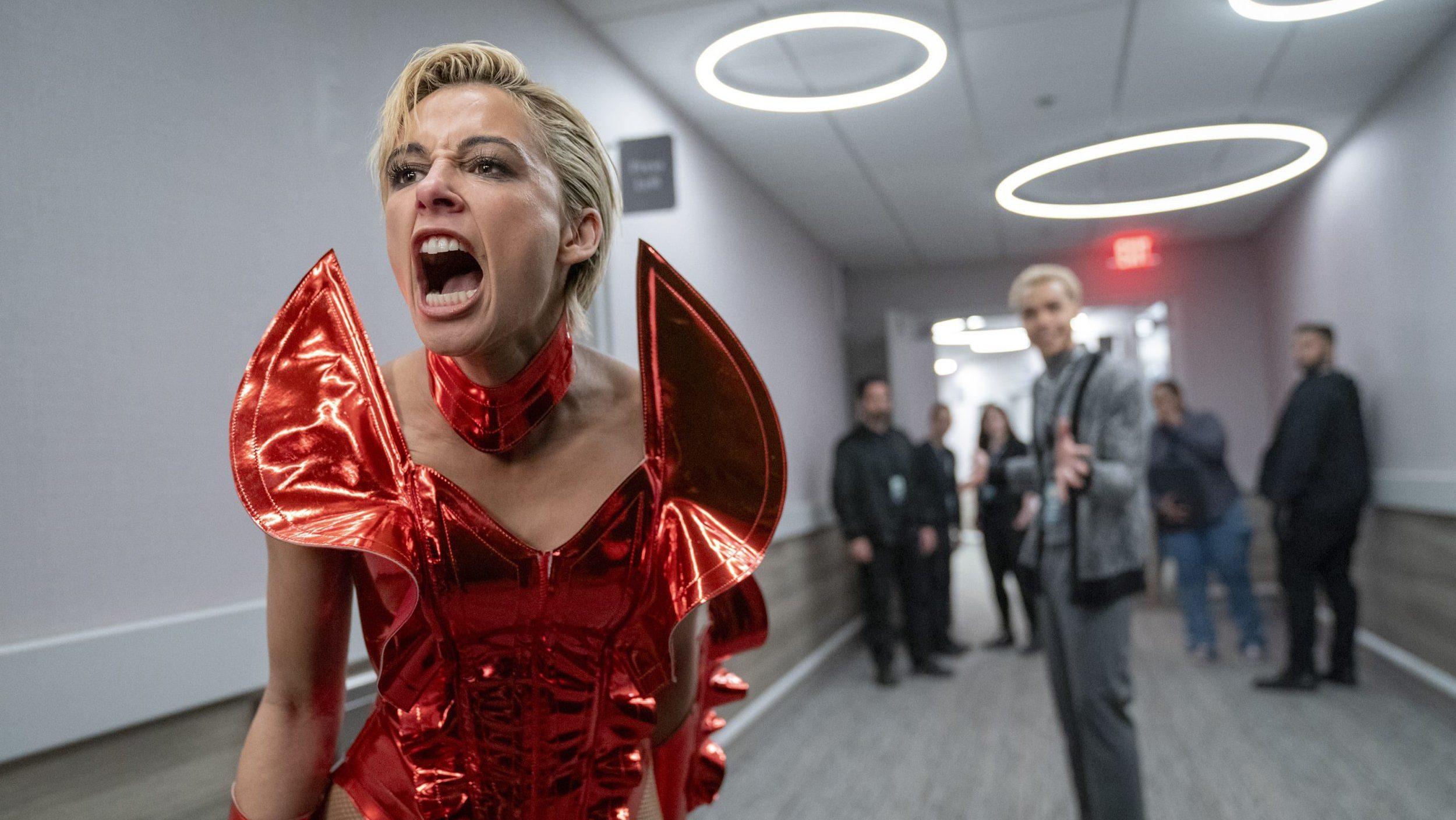 An image from the film Smile 2. It features a woman (Naomi Scott) wearing a poster outfit screaming in a backstage area.