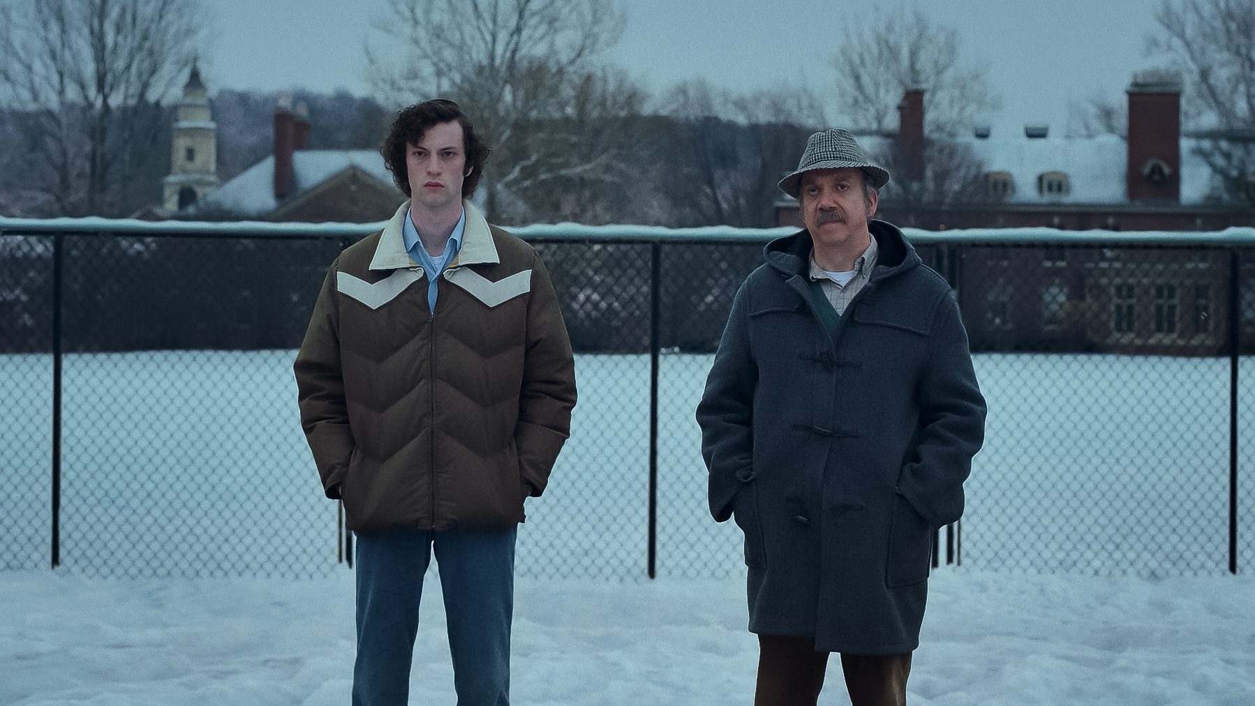 An image from the film The Holdovers. It features two men (Dominic Sessa and Paul Giamatti) standing outside in the snow.