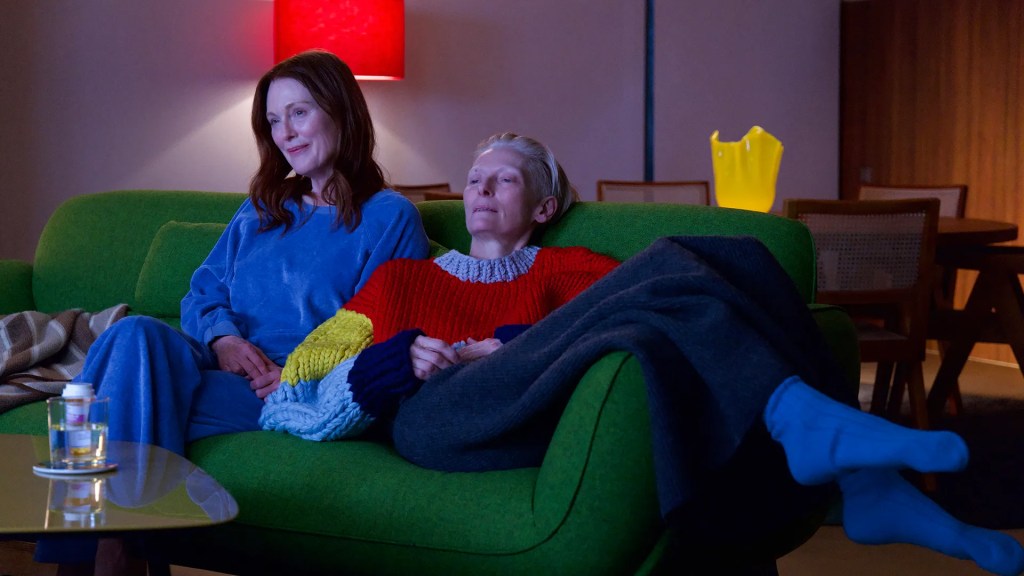 An image from the film The Room Next Door. It features two women (Julianne Moore and Tilda Swinton) sitting on a bright green sofa together.