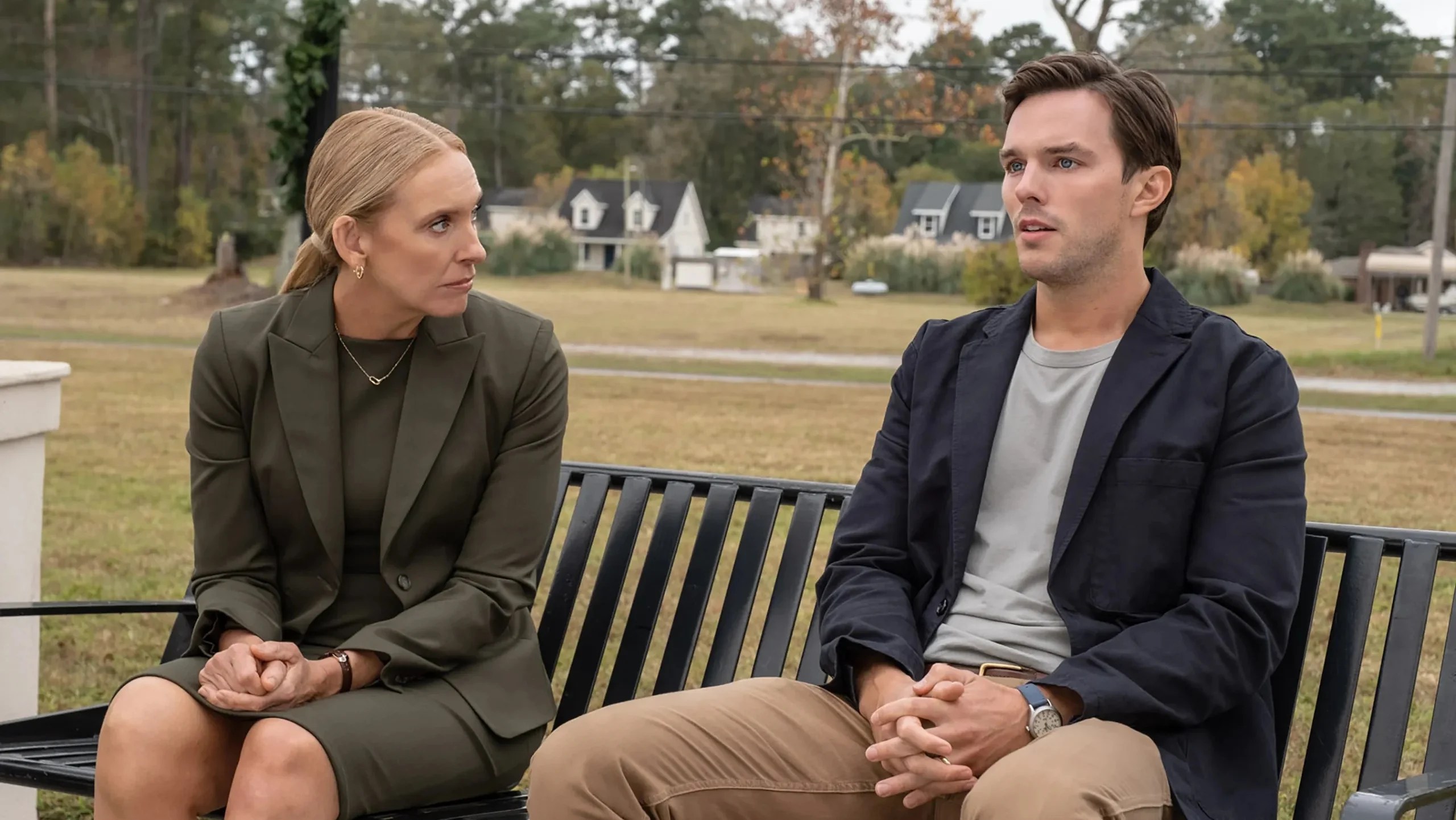 An image from the film Juror #2. It features a man (Nicholas Hoult) and a woman (Toni Collette) sitting on a bench outside a courtroom. 
