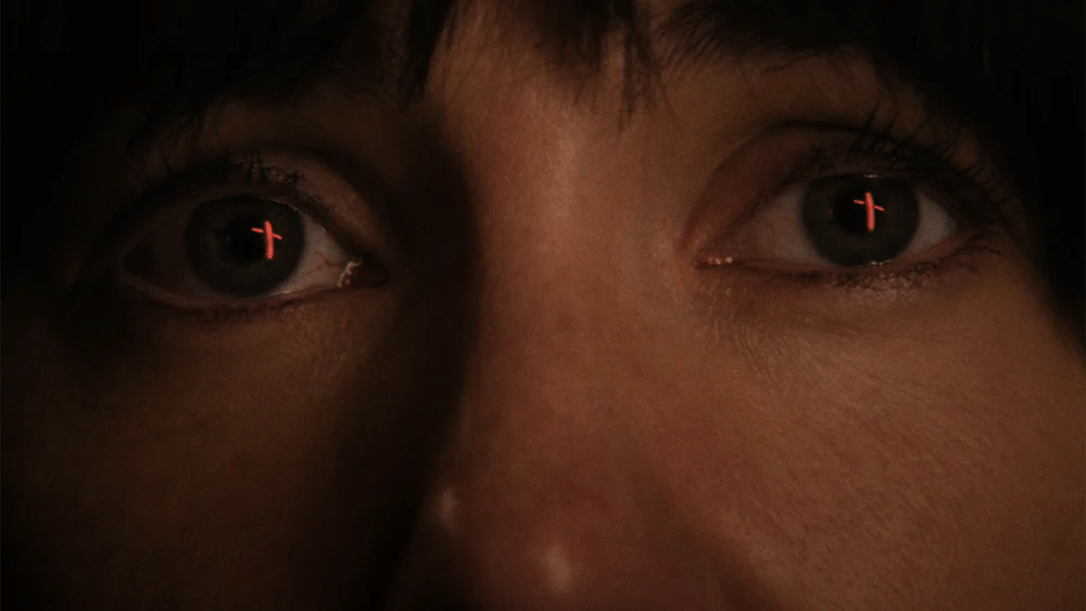 An image from the film Fréwaka. It features a close up of a woman (Clare Monnelly) Red crosses can be seen in the reflection of her eyes.