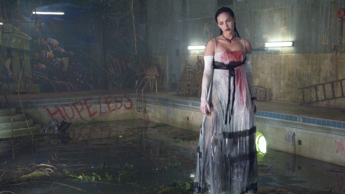 An image from the film Jennifer's Body. It features a woman (Megan Fox) levitating above an unused pool. She is wearing a prom dress which is dripping in water and has blood stains down the front of it. 