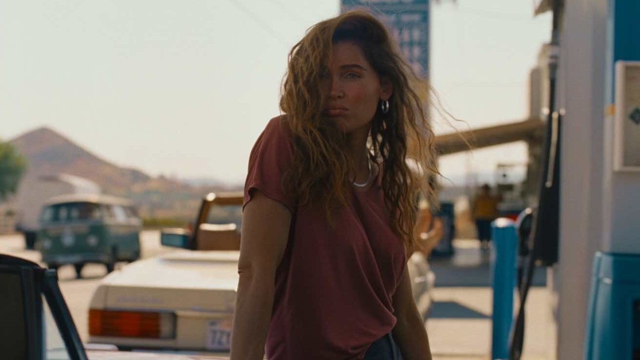 An image from the film Monica. It features a woman (Trace Lysette) leaning on her car as it fills up with fuel. 