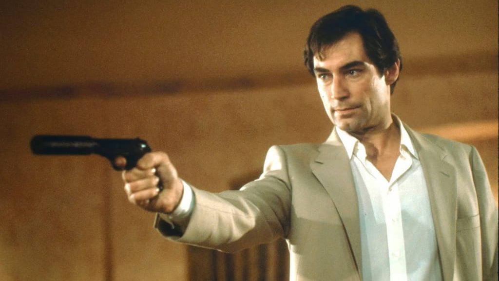 An image from the film The Living Daylights. It features a man (Timothy Dalton) holding a pistol with a silencer attached. He is aiming the weapon in front of him. 